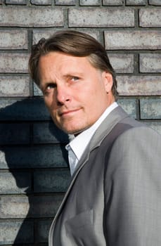 a handsome pensive looking businessman is standing in front of a brick wall.