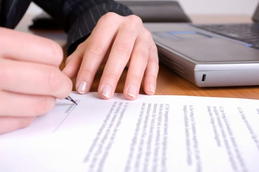 Hands signing a contract with laptop in background