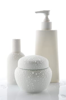 Three white cosmetic bottles with water drops, stand on a white background