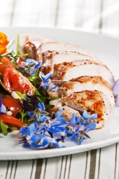 Grilled chicken breast served with salad and garnished with edible flowers