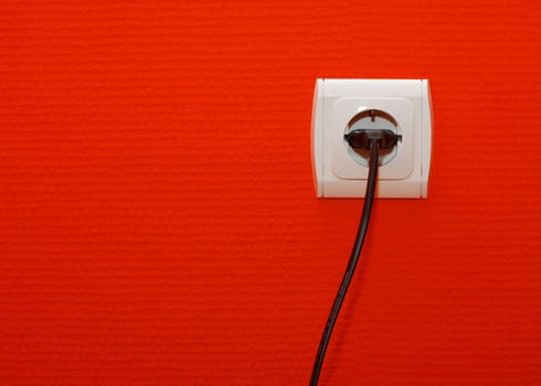 Electric outlet on red wall with cable connected