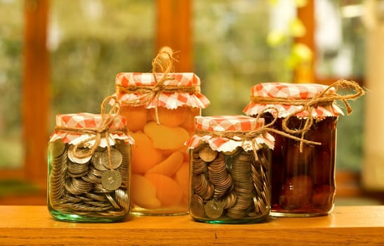 Save when you have plenty - money saving concept with canned fruits and money in glass jars