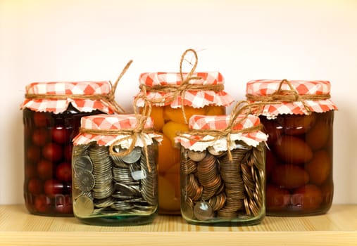 Savings concept with canned fruit and coins in glass jars on the shelf