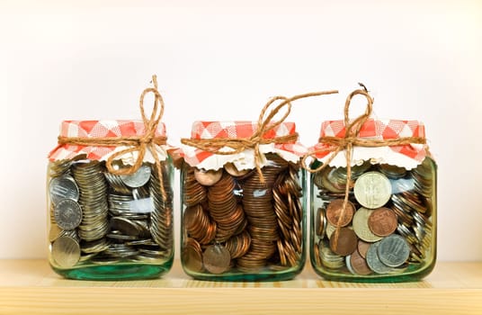 Saving money concept with coins put away in glass jars on a shelf