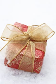A close-up of a Christmas gift with red colored wrapping and a decorative bow resting on white snowflakes.