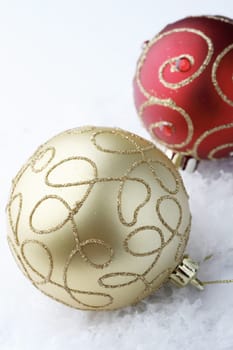A close-up of two, red and gold colored, Christmas bauble decorations resting on white snowflakes.
