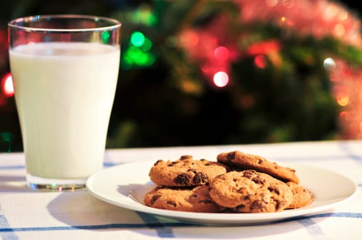 Plate of cookies and glass of milk near Christmas tree