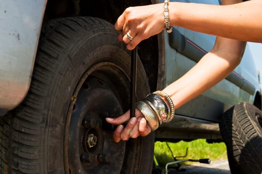 Woman, loosening the bolts on a wheel to change a flat tire
