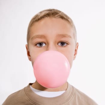 A young boy is chewing bubble gum and blowing a bubble.  He is looking at the camera.  Vertically framed shot.
