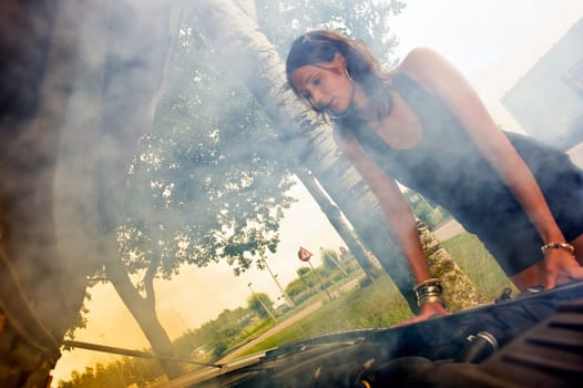 Pretty woman looking sad at the smoke coming from the blown engine of her car