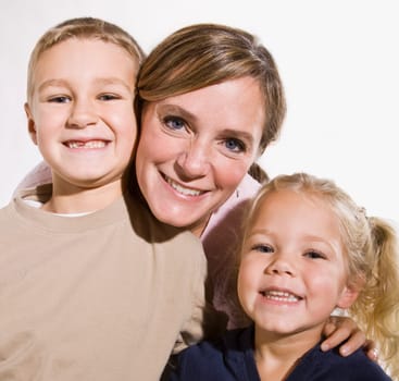 A young mother is standing with her two young children and they are smiling at the camera.  Square framed shot.