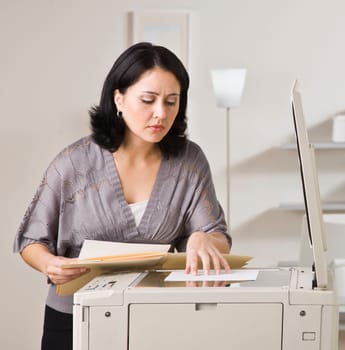 Attractive asian woman making copy on copy machine in office. Looking at paper on machine. Square.