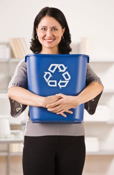A businesswoman is holding a recycling basket and smiling at the camera.  Vertically framed shot.