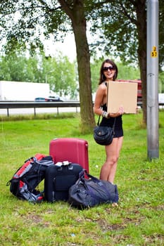Young woman hitch hiking with a lot of luggage along a motorway all by herself