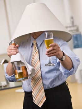 Male wearing lampshade on his head, holding Champagne bottle and glass in hands. Vertical