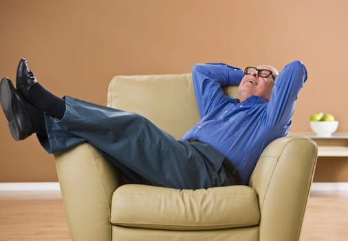 Attractive male senior laughing, while sitting on an overstufffed chair. Looking at the ceiling. Horizontal.