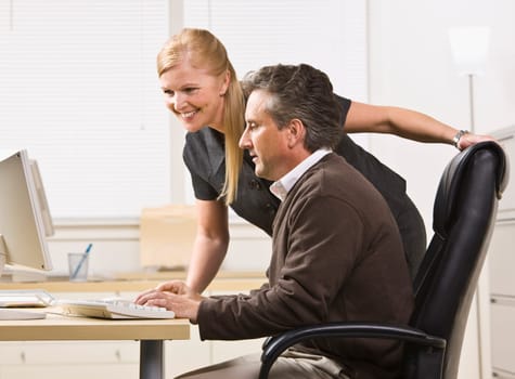 Attractive male and female working on computer. Female standing over male sitting at desk. Looking at computer. Horizontal