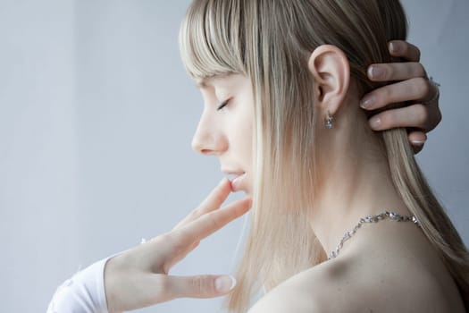 young blonde sexy girl posing with white gloves on her hands and her eyes closed