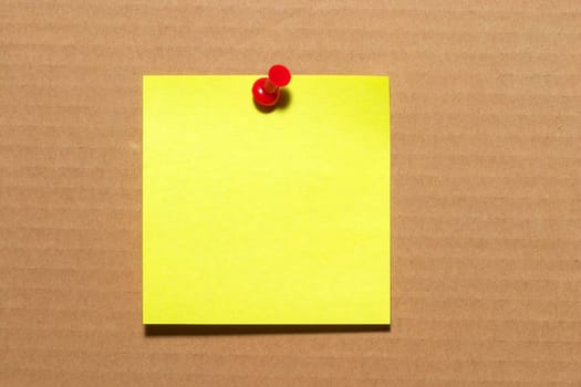 Yellow sticker note with a red push-pin over cardboard