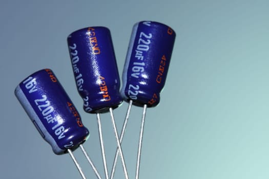 Three electrolytic capacitors on a blue background.