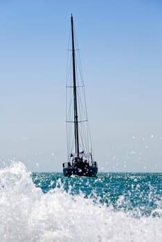 yacht drifting in the sea with sails down. Splash of water wave in foreground and blue sky in background