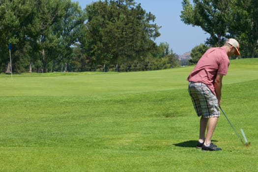 A Man golfing swinging his club toward the tee