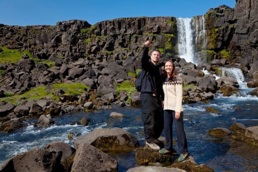 A young couple crossing a mountain stream while out walking together. Shot on location in Iceland.