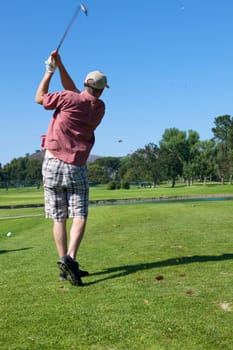 A Man golfing swinging his club toward the tee