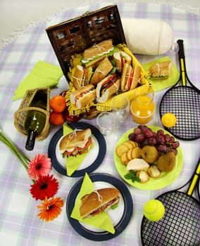 Selection of food for a picnic with a hamper, basket, fruit, wine and tennis racquets.