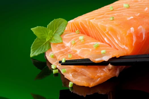 a piece of fresh salmon with basil leaves and chopstick