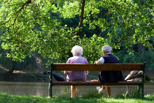 Aged couple enjoy spring morning on the bench near lake in the park