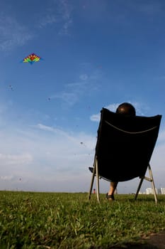 A man flying a kite wth a relax sitting position.