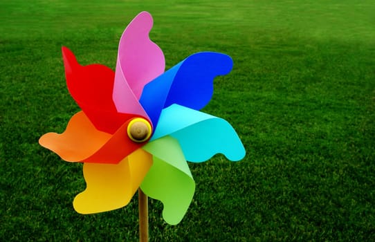 A multicolored pinwheel stands with a beautiful green grassy field