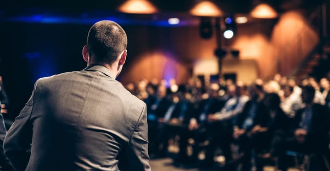 Speaker giving a talk on corporate business conference. Unrecognizable people in audience at conference hall. Business and Entrepreneurship event.