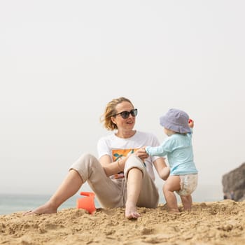 Mother playing his infant baby boy son on sandy beach enjoying summer vacationson on Lanzarote island, Spain. Family travel and vacations concept