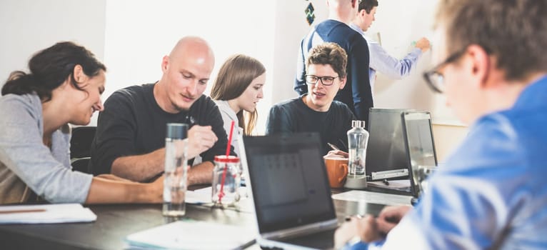 Startup business and entrepreneurship problem solving. Young AI programmers and IT software developers team brainstorming and programming on desktop computer in startup company share office space.