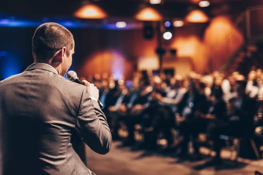 Speaker giving a talk on corporate business conference. Unrecognizable people in audience at conference hall. Business and Entrepreneurship event.