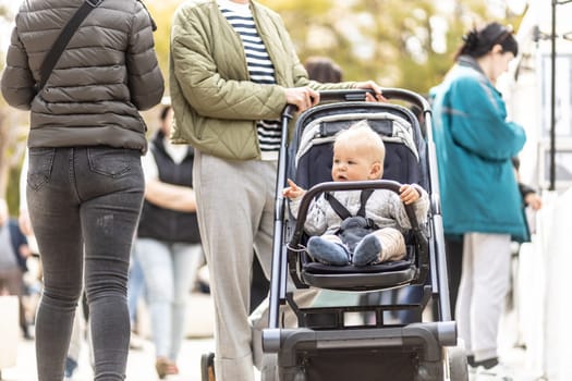 Mother walking and pushing his infant baby boy child in stroller in crowd of people wisiting sunday flea market in Malaga, Spain
