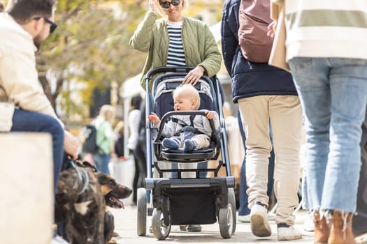 Mother walking and pushing his infant baby boy child in stroller in crowd of people wisiting sunday flea market in Malaga, Spain