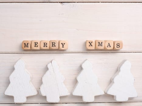 Small wooden blocks with Merry Xmas and white wooden Christmas tree on a wooden table