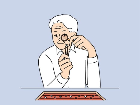 Elderly man jeweler examines diamond through magnifying glass checking gems for authenticity. Gray-haired worker in jewelry workshop chooses diamond to create necklace or engagement ring.