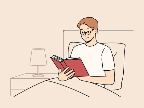 Man reads book before bedtime, sitting in bed at night and enjoying plot of fantasy novel. Smart young guy student preparing for exam in bed studying textbook with educational information