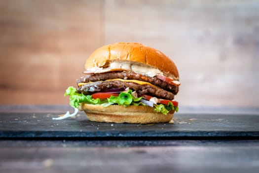 beef burger with sesame lettuce bun tomato cheddar cheese on black background