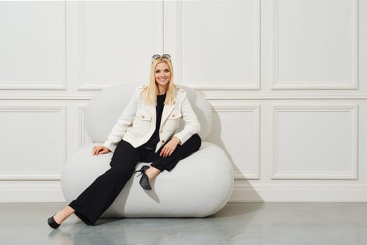 Happy woman in wide trousers, blouse and jacket posing in bright room