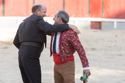 March 26, 2023 Lisbon, Portugal: Tourada - two smiling elderly men hug - forcado and cavaleiro. Mid shot