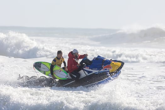 14 march 2023 Peniche, Portugal: Surf Competition Winner Participant - two men one holding surfboard and another riding a jet ski with a Red Bull sticker on the surface. Mid shot