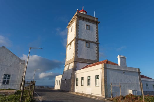 The building of the coastal lighthouse on a hill by the sea against the background of the blue sky. Mid shot