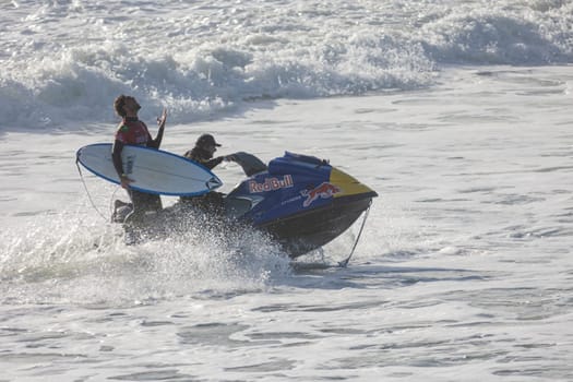 14 march 2023 Peniche, Portugal: surf competition - two men one holding surfboard and another riding a jet ski with a Red Bull sticker on the surface. Mid shot