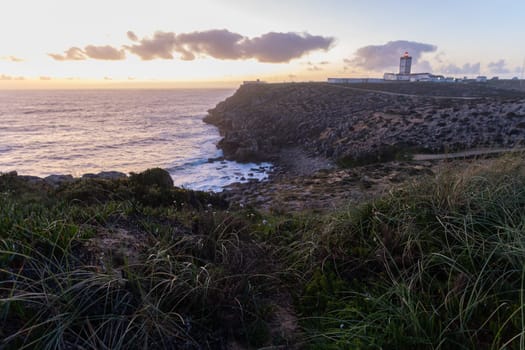 A lighthouse on an island on a hill by the sea at early sunset. Mid shot