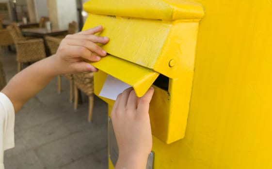 Boy putting a letter in the spanish yellow traditional mailbox. Selective focus